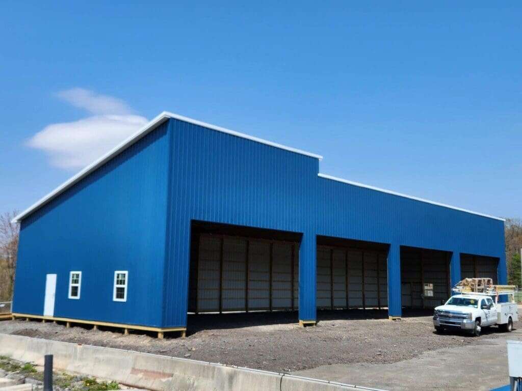 Bold blue post-frame utility building with multiple large open bays and utility truck on site